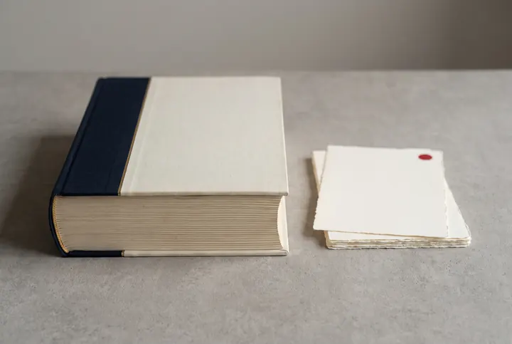 Bound file with a navy cloth spine next to a small stack of blank sheets