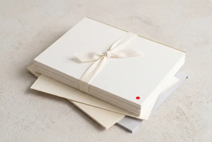 Stack of paper sheets tied with an ivory ribbon, resting on layered ivory and grey sheets